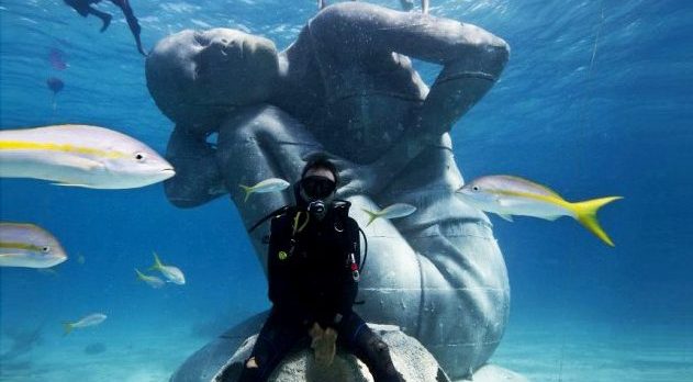 A diver with a reefball by an underwater statue